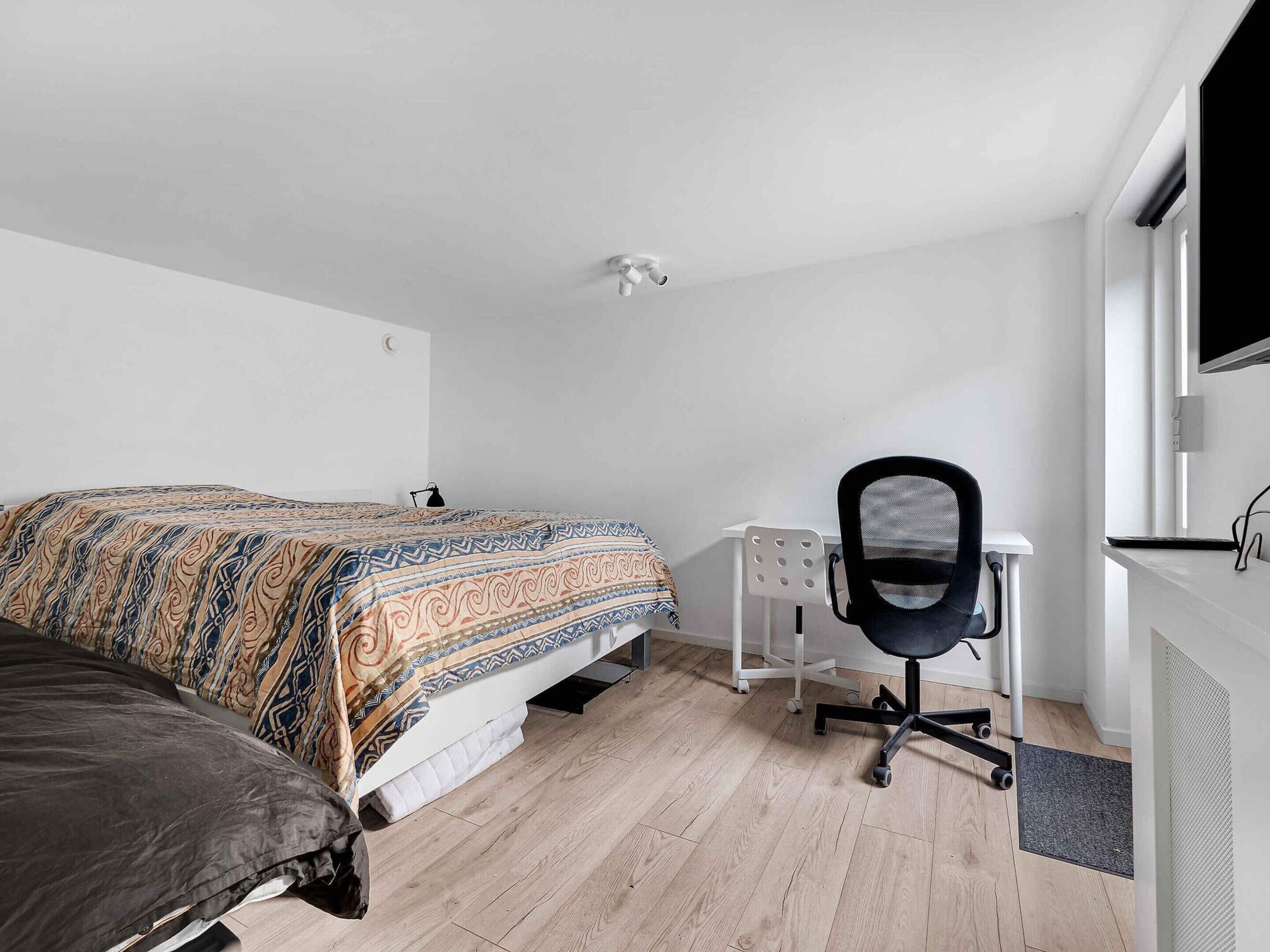 Um quarto com uma cama, uma escrivaninha e uma cadeira.