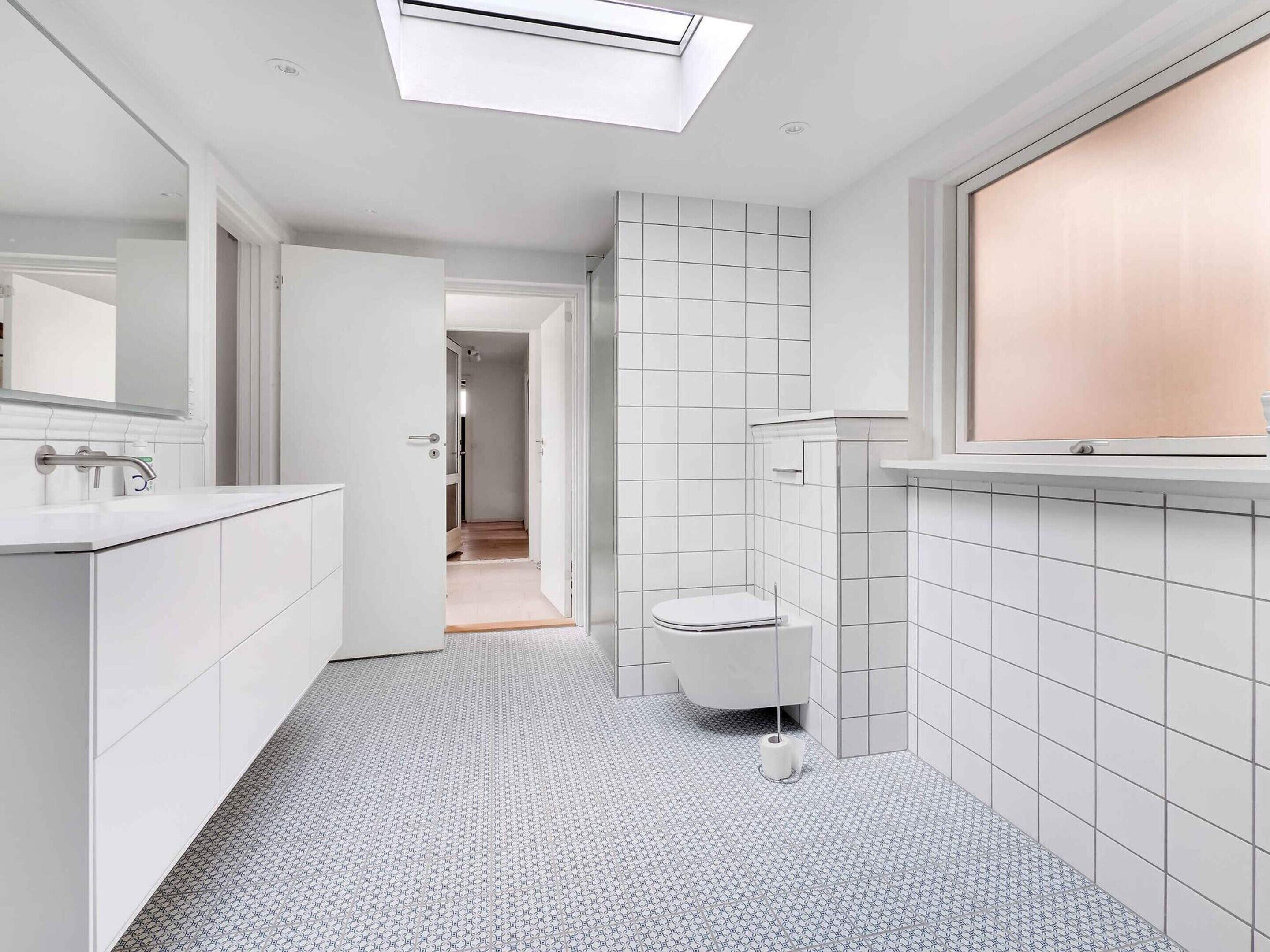 Ein modernes Badezimmer mit Oberlicht, weißen Fliesen, Toilette und Waschbecken.