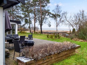 Una terraza con mobiliario exterior, una parrilla y vista a la playa.