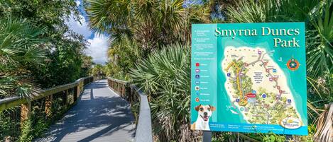 Un paseo marítimo de madera que atraviesa un parque, con un mapa y un cartel informativo.