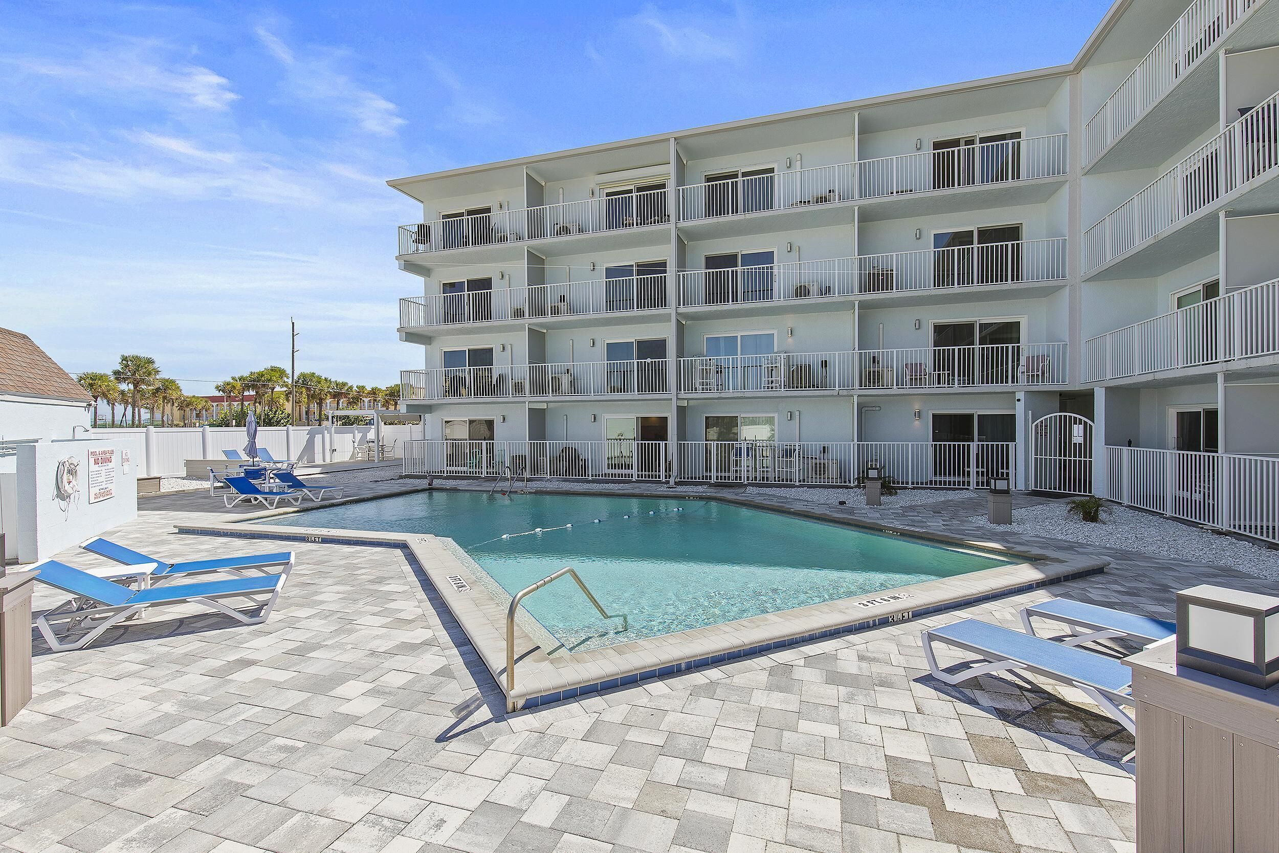 A multi-story hotel with a swimming pool, outdoor seating, and a clear sky.