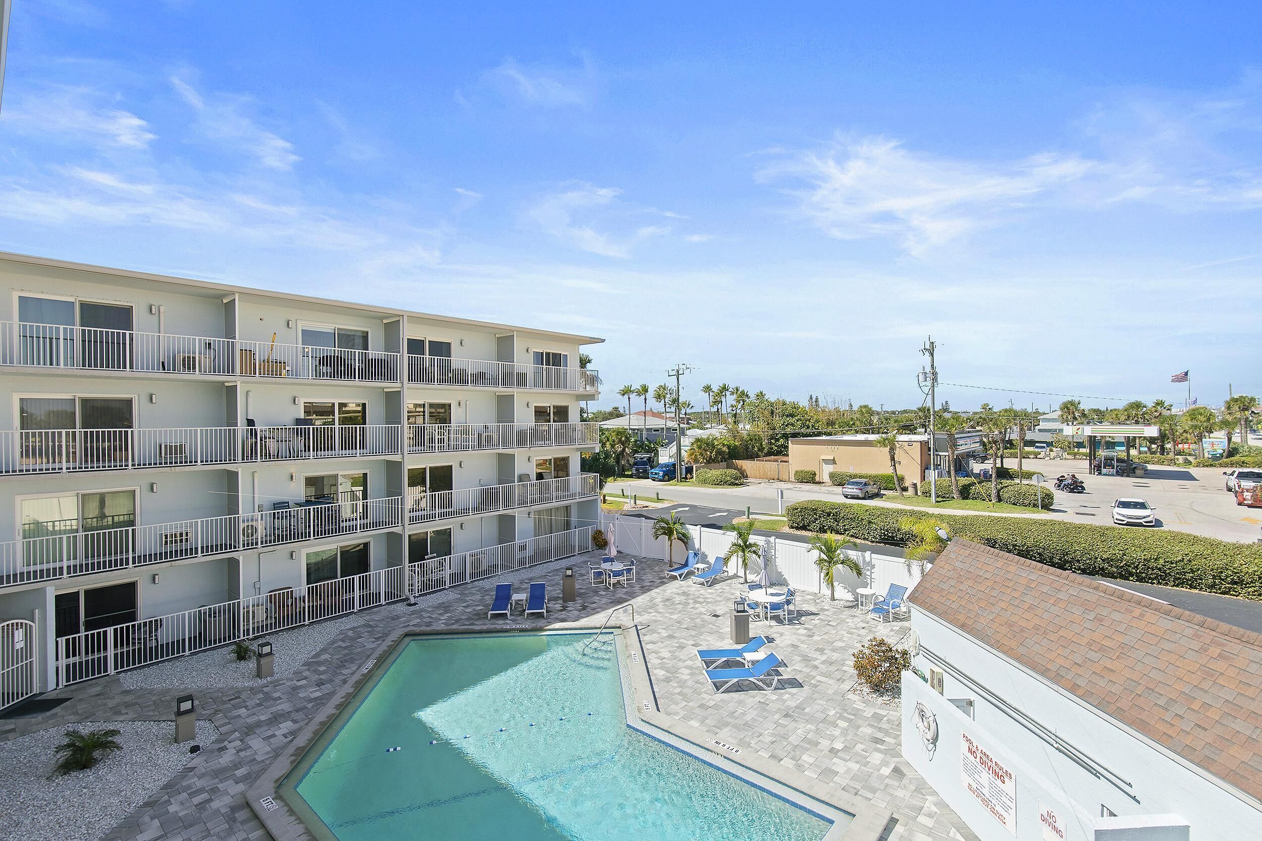 A multi-story hotel with a swimming pool, outdoor seating, and a view of the surrounding area.