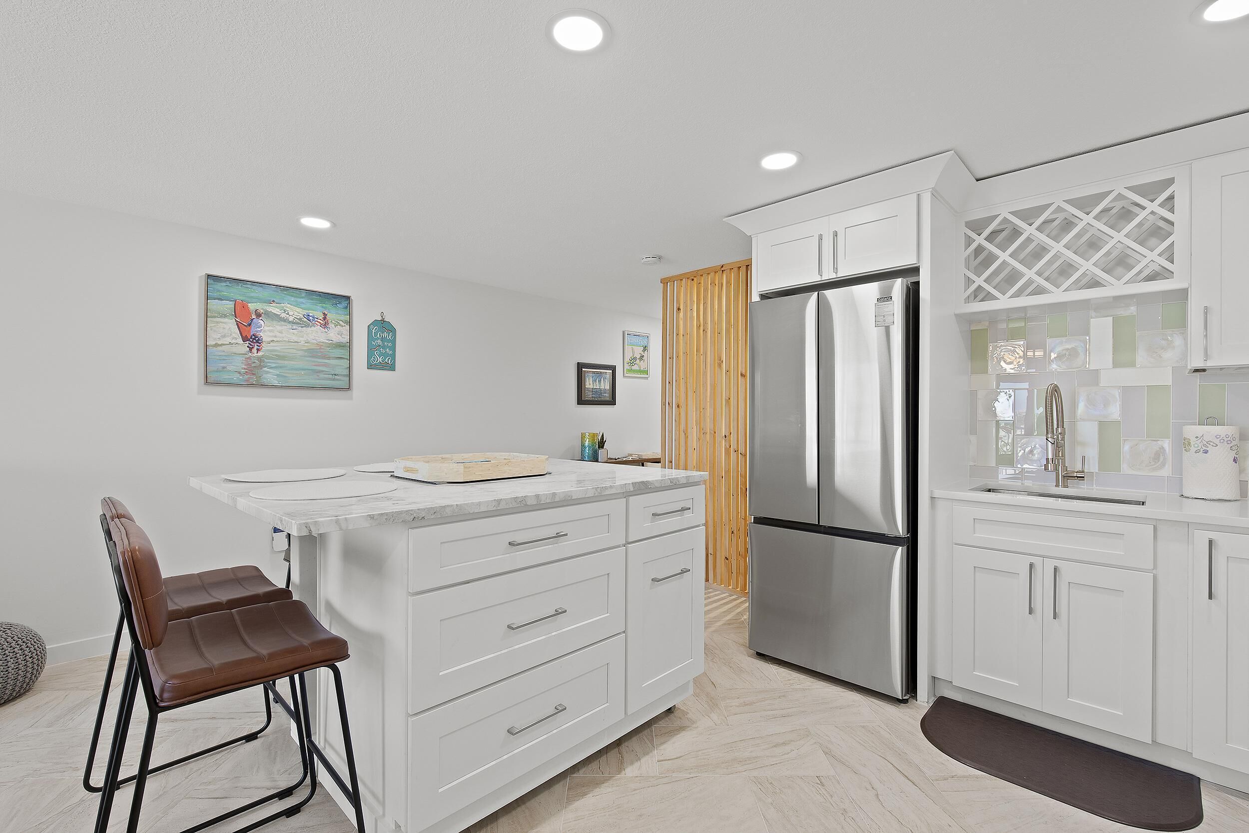 A modern kitchen with white cabinets, a stainless steel refrigerator, and a wooden accent wall.