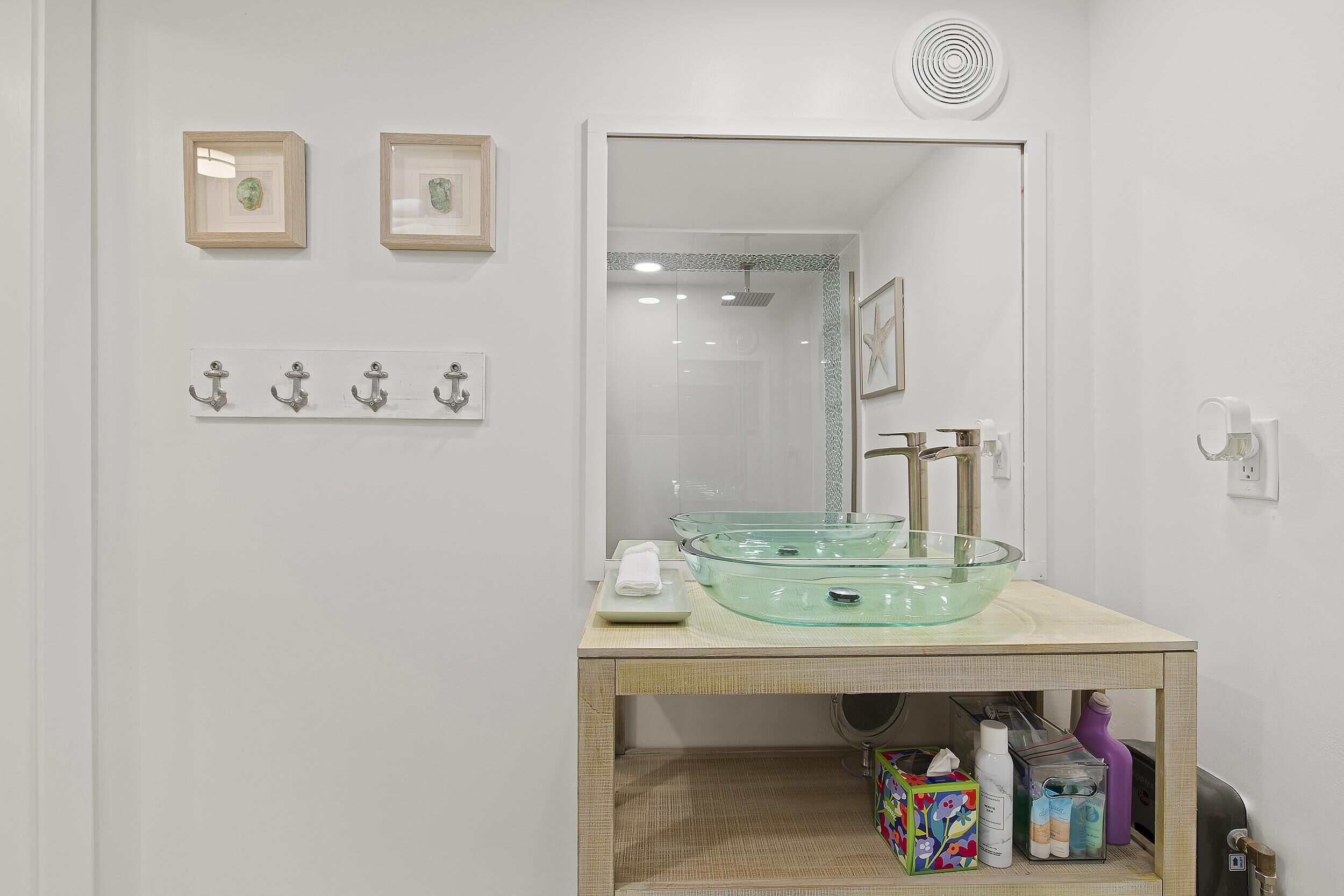 A bathroom with a glass bowl sink, a mirror, and a shelf with toiletries.