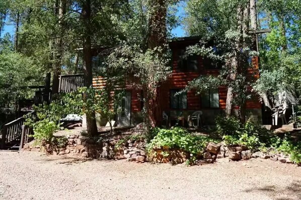 A rustic log cabin with a stone foundation, surrounded by dense forest.