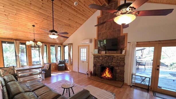 A spacious living room with a fireplace, leather sofas, a television, and a ceiling fan.
