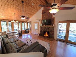 A spacious living room with a fireplace, leather sofas, a television, and a ceiling fan.