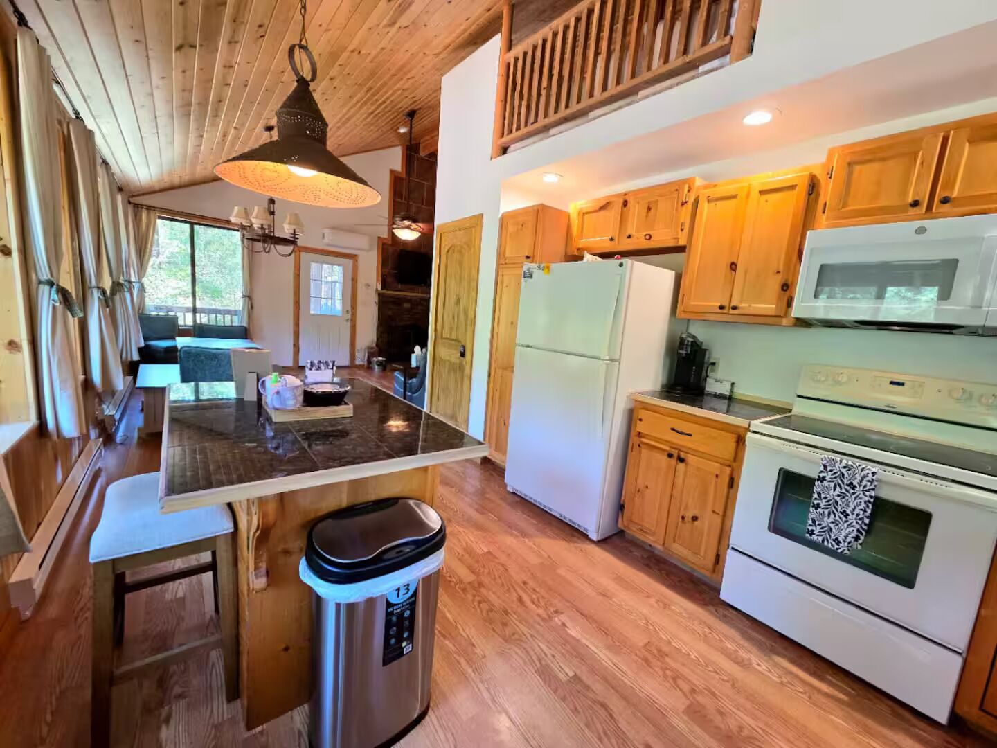 A kitchen with wooden cabinets, a stainless steel trash can, a refrigerator, and a microwave.