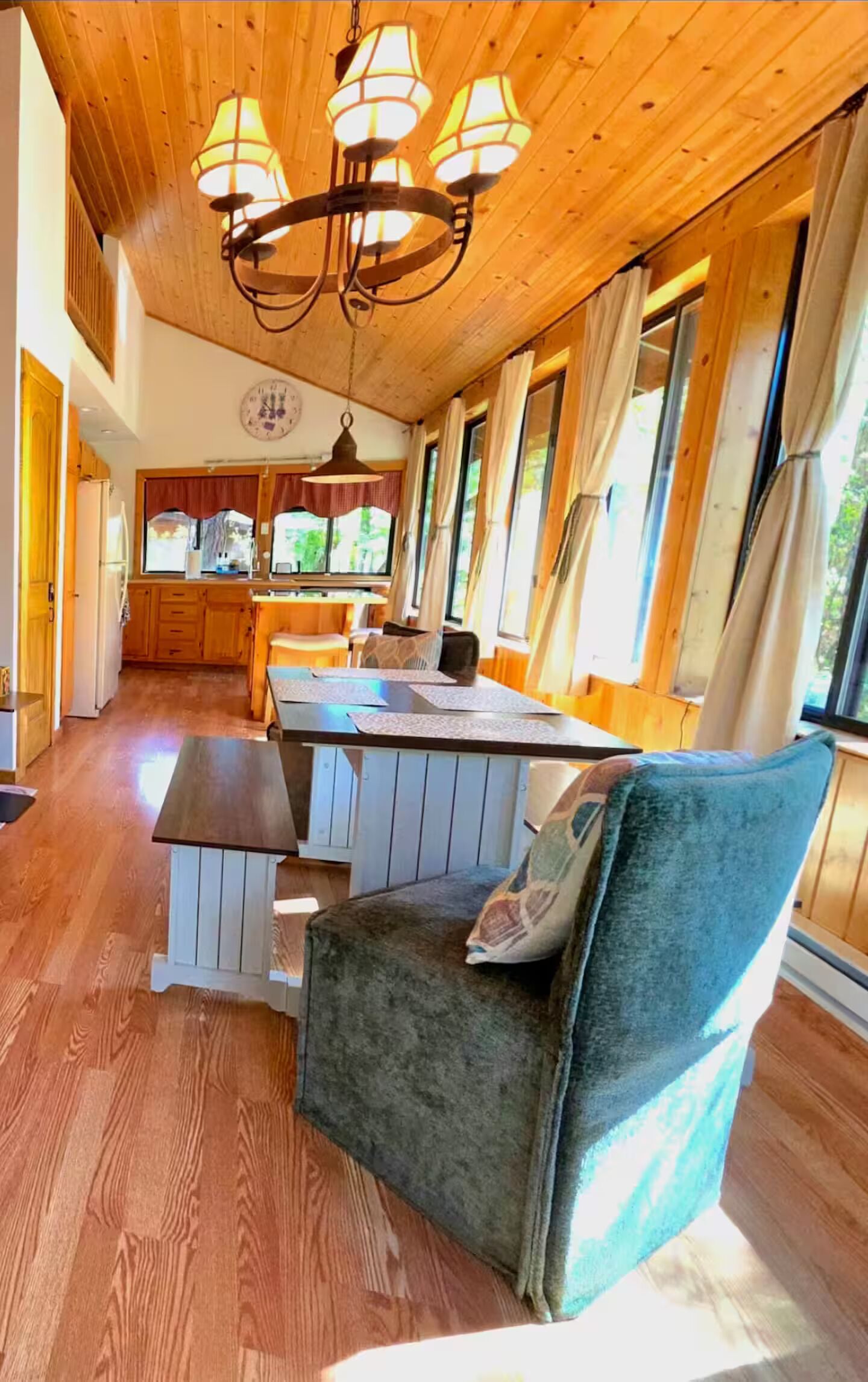 A cozy interior with a wooden ceiling, a dining area with a table and chairs, and a kitchen in the background.