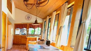 A cozy interior with a wooden ceiling, a dining area with a table and chairs, and a kitchen in the background.