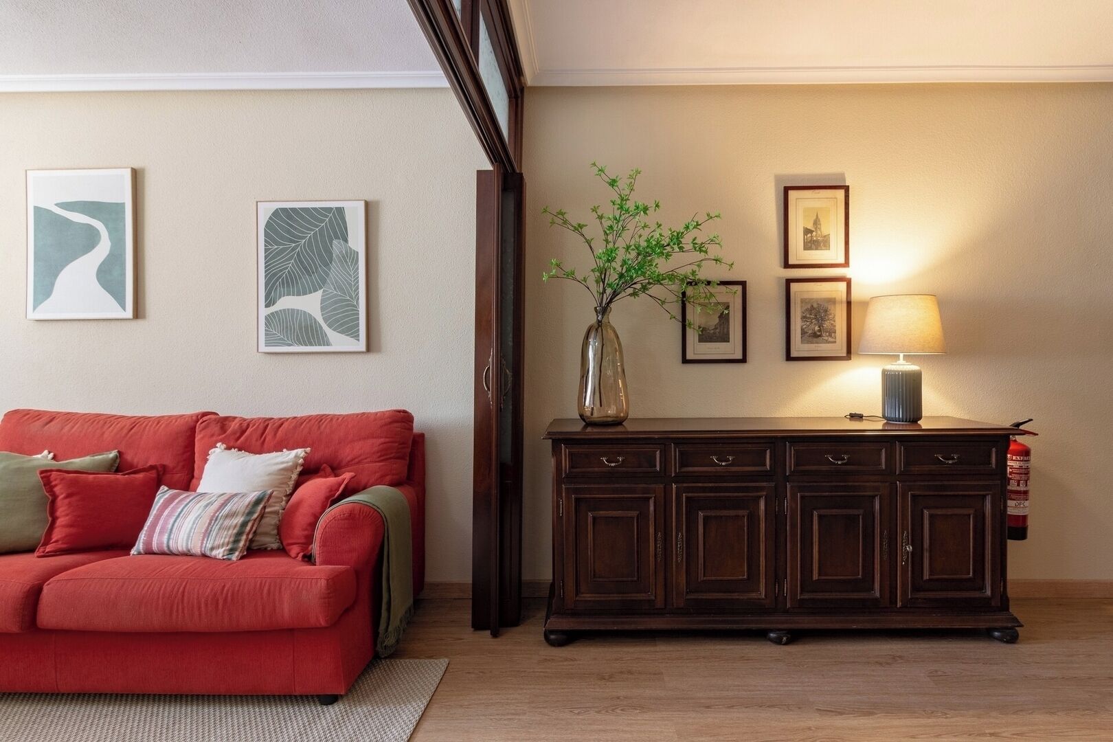 Een woonkamer met een rode bank, een donker houten kast en kunstwerken aan de muur.