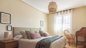 Un dormitorio con cama, mesitas de noche, un piano y una ventana con cortinas.