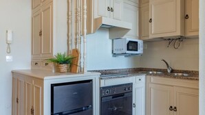 Una cocina compacta con muebles blancos, un microondas integrado, un refrigerador negro y piso de madera.