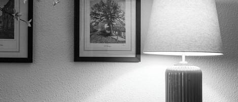 A black and white photo of a wall with three framed pictures and a lamp.