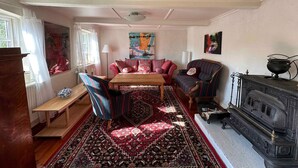 A cozy living room with a sofa, armchairs, a wooden coffee table, and a patterned rug. There is a fireplace with a decorative pot on top.