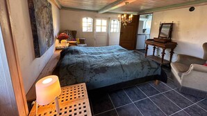 A bedroom with a bed, a dresser, a chair, a lamp, a chandelier, and a window.