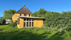 A yellow house with a red roof, surrounded by green grass and trees.