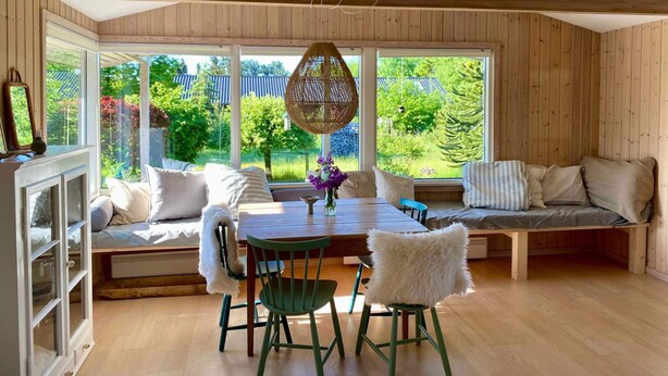 A cozy room with a wooden ceiling, large windows, a dining table, and a seating area. - 5 Star Holiday Home in Hundested (Hundested)