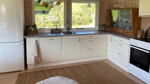 A kitchen with wooden cabinets, a refrigerator, an oven, and a window with a view of greenery. - 5 Star Holiday Home in Hundested (Hundested)