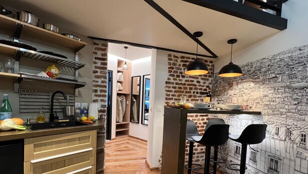 A modern kitchen with wooden cabinets, a black countertop, and a brick wall mural. - Rue de la Voûte - Mobility lease (París)