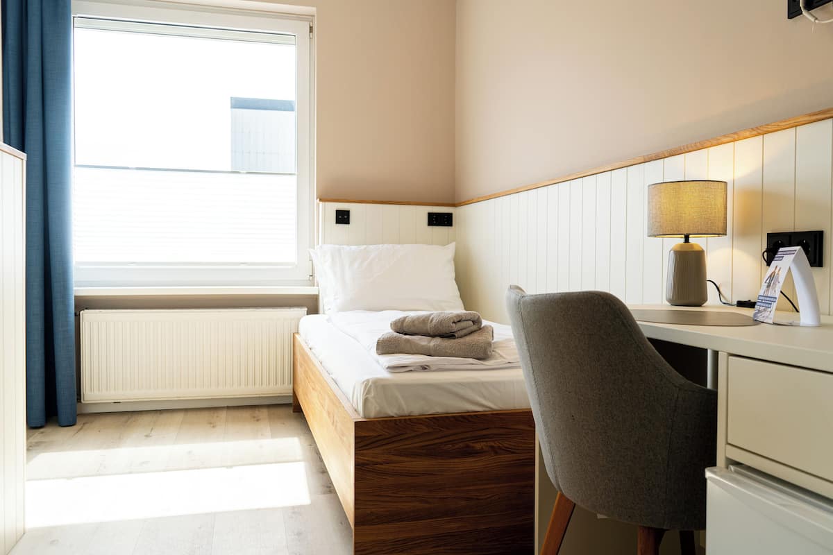 Una camera d'albergo con un letto, una scrivania, una sedia, una lampada e una finestra.