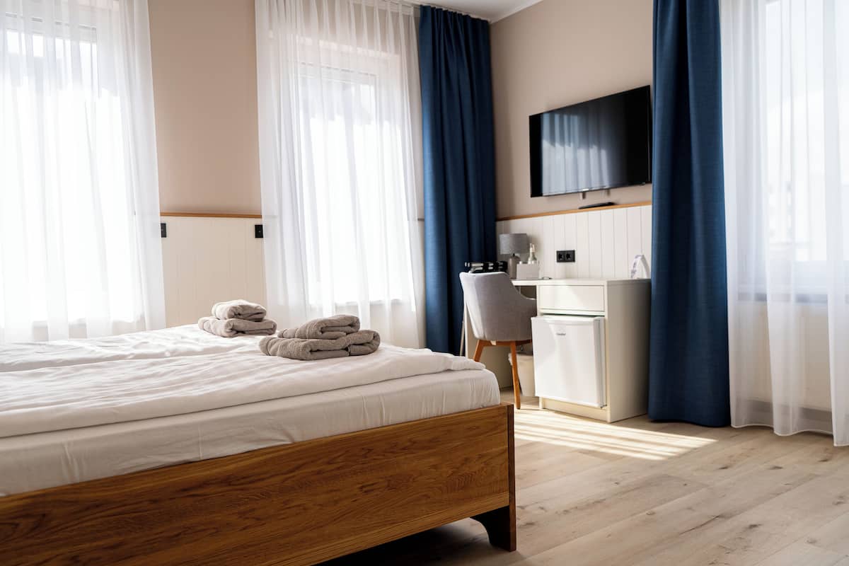 Una camera d'albergo con un letto di legno, una scrivania, una sedia e una TV a schermo piatto appesa al muro.