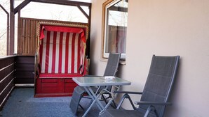 A small outdoor seating area with a glass table and two chairs, a red and white striped awning, and a wooden deck. - Hotel Seebrise Grömitz (Groemitz)