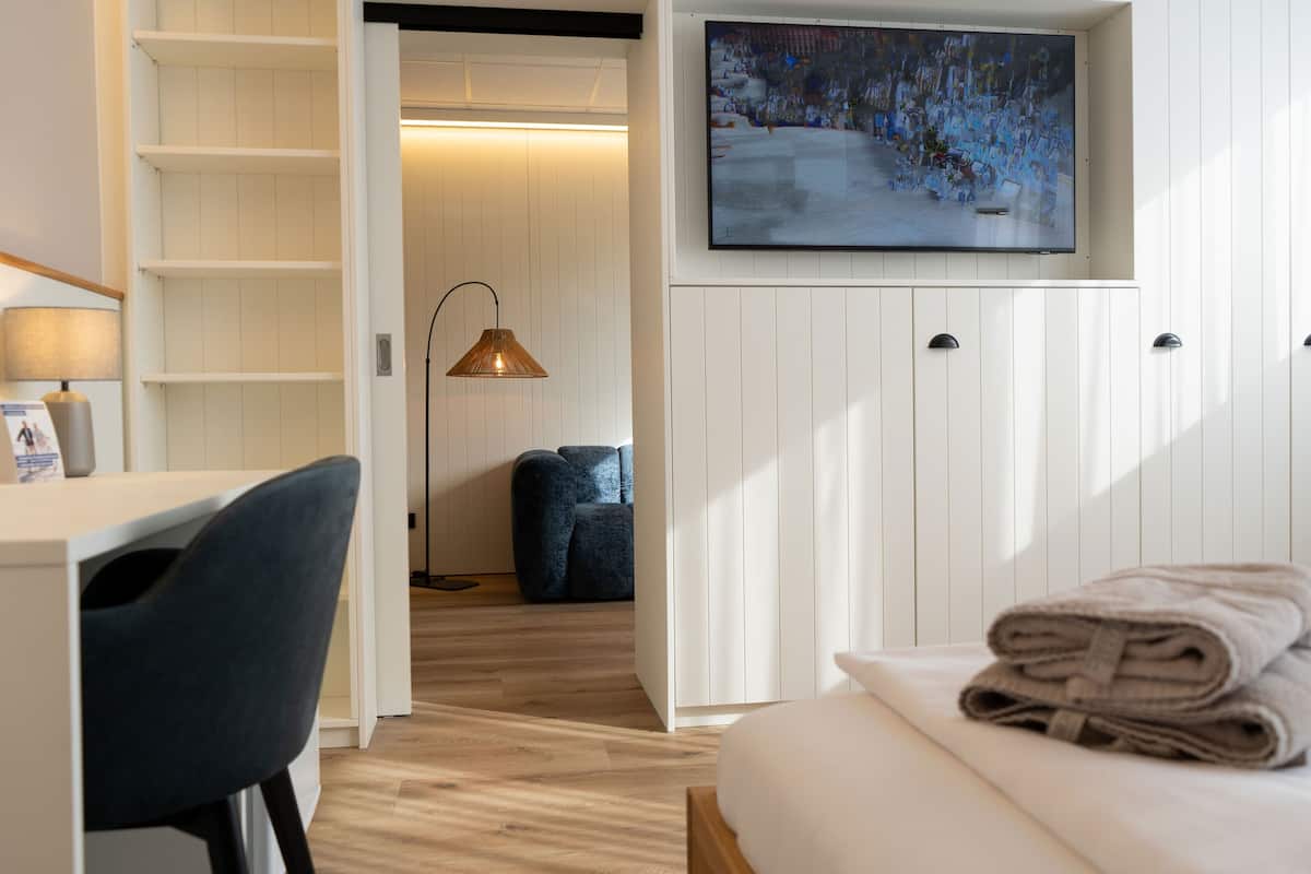 Una camera d'hotel con un letto, una scrivania con una sedia, una TV a parete e una lampada.