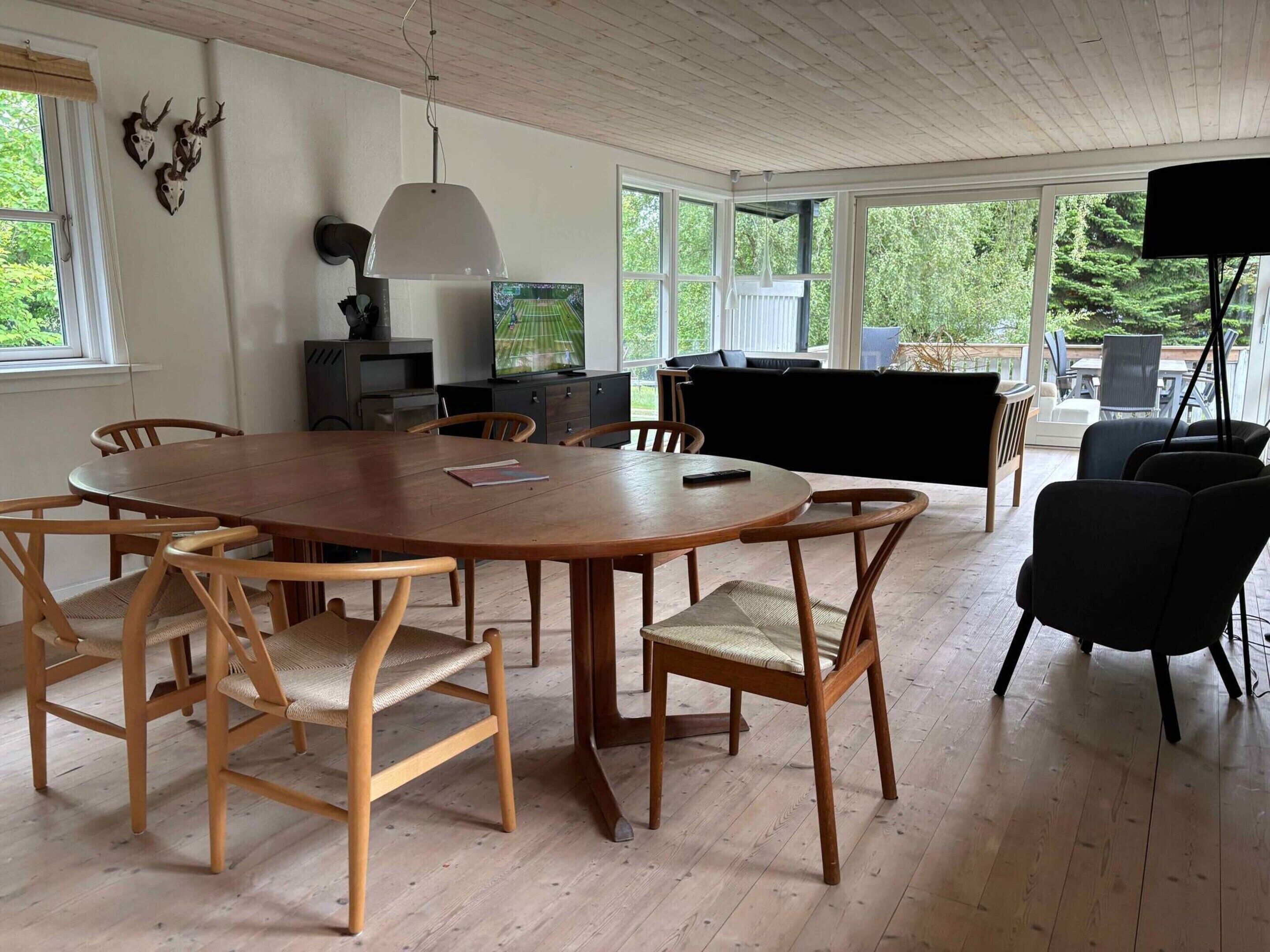 Una habitación amplia con una gran mesa de comedor de madera rodeada de sillas, un piano y un televisor.