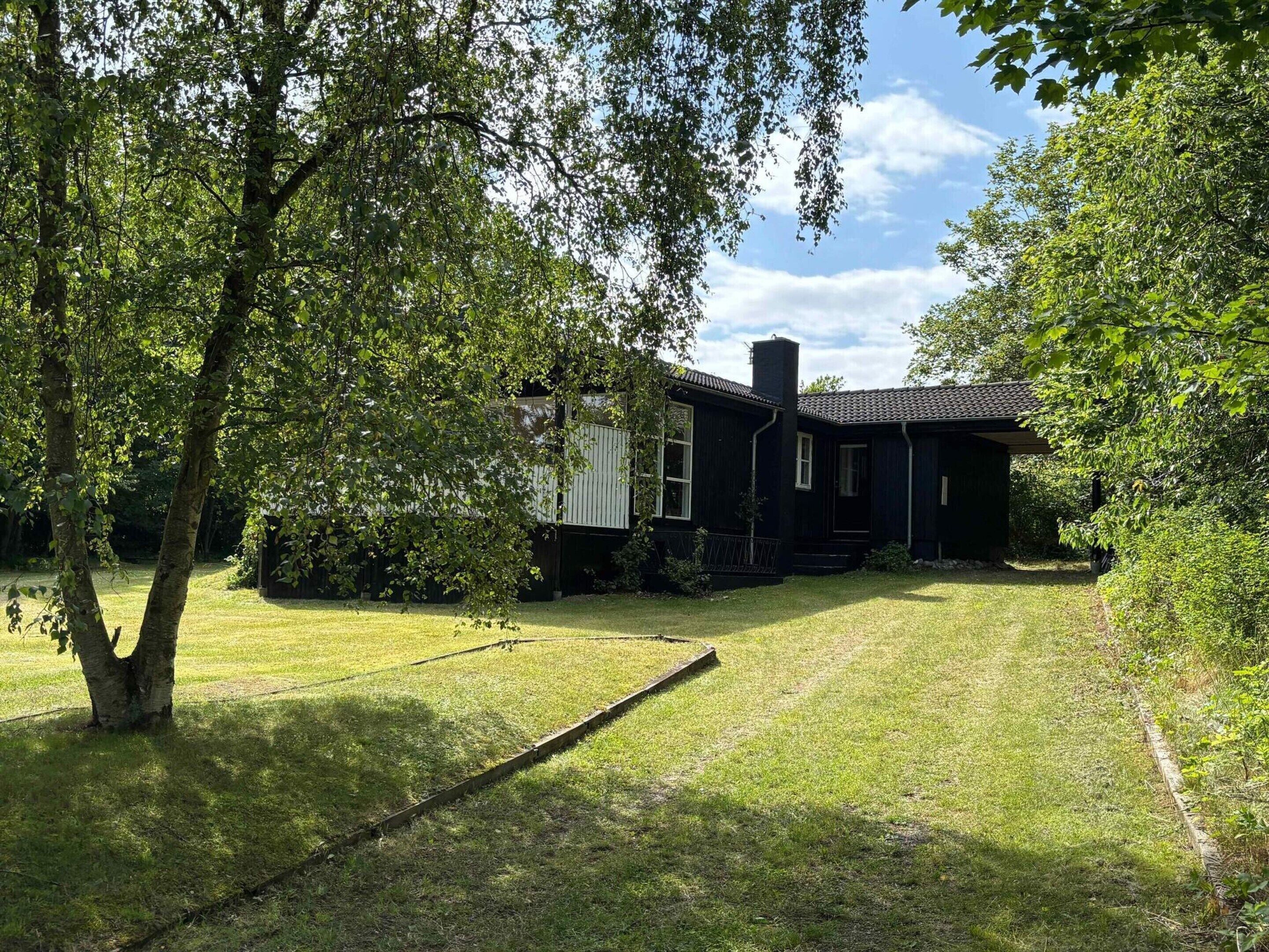 A black house with a chimney, surrounded by a well-maintained lawn and trees.