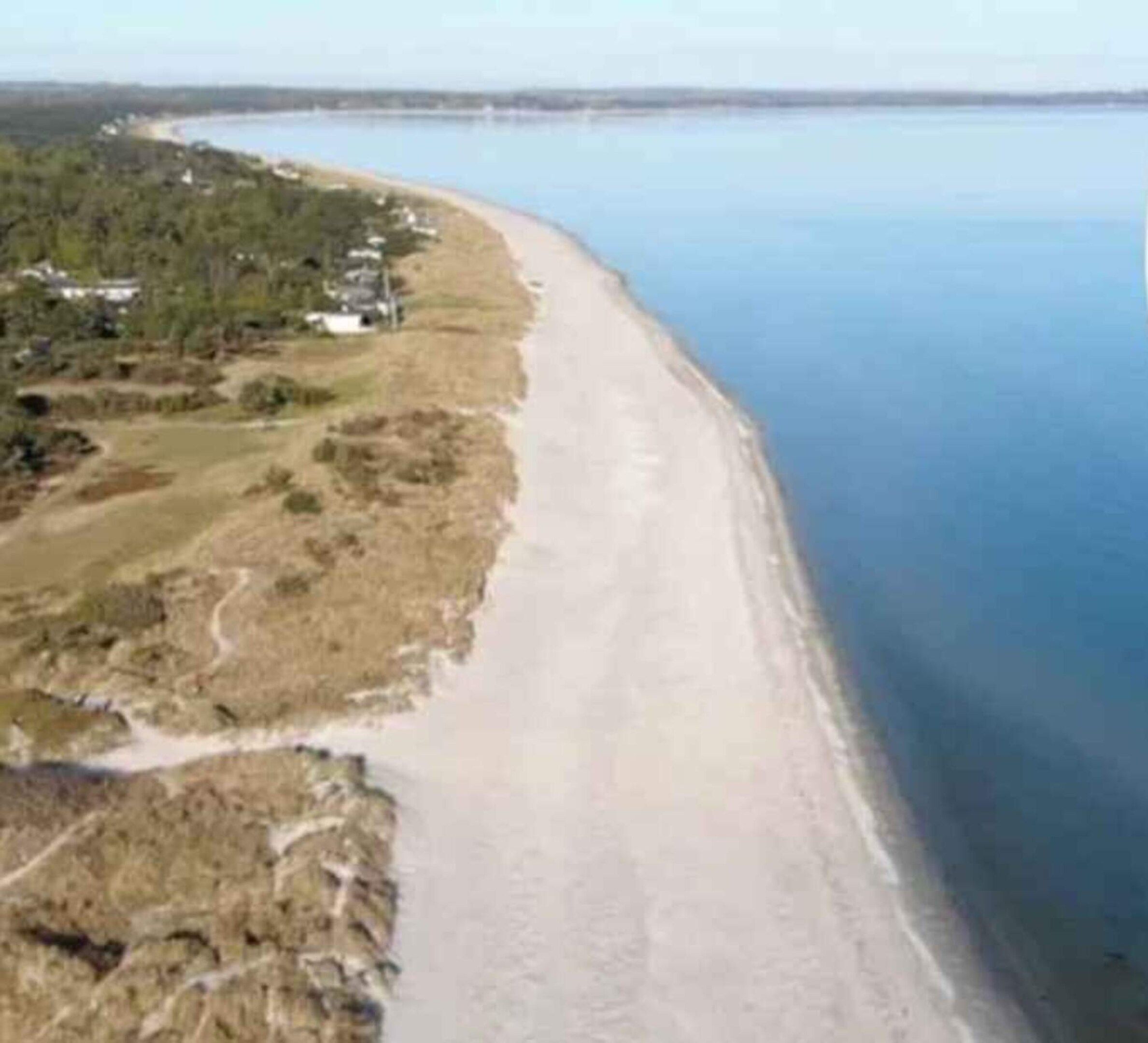 Paisagem costeira com uma praia e uma estrada serpenteando pela costa.