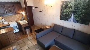 Un espace de vie compact comprenant un coin cuisine, un canapé et une grande fenêtre donnant sur un paysage verdoyant.