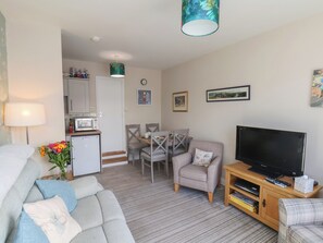 A compact living space with a sofa, a television, a dining area, and a kitchenette. - Farriers Yard (Whitby)