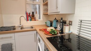A compact kitchen with a sink, stove, and a window above the countertop. - Farriers Yard (Whitby)