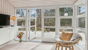 A room with a television, a wicker chair, and a large glass door leading outside. - 5 Star Holiday Home in Nykobing Sj (Nykobing Sjaelland)