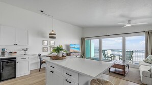 Una cocina moderna con armarios blancos, una isla central y un comedor con vistas al mar.