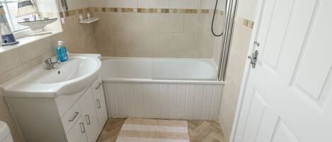 Un baño con un lavabo blanco, inodoro y bañera. Hay una alfombra a rayas en el suelo y un cabezal de ducha sobre la bañera.