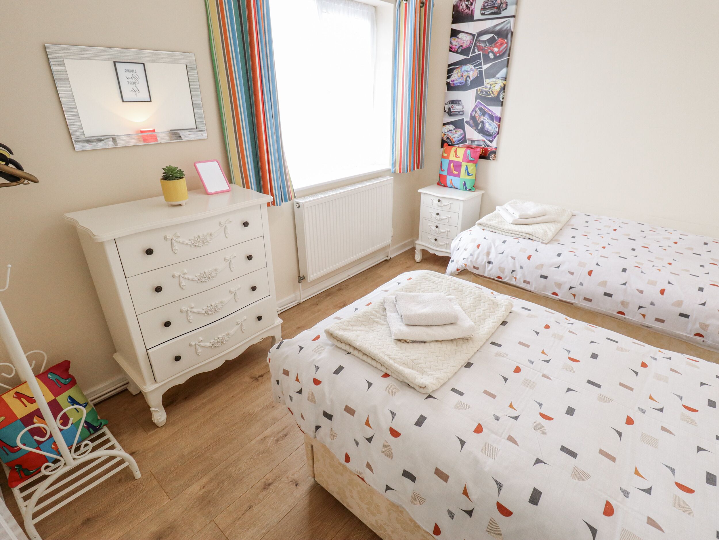 A bedroom with two single beds, a dresser, a radiator, and a window with curtains.