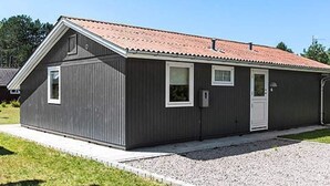 A single-story, dark-colored metal building with a red-tiled roof, a front door, and two windows. - 5 Star Holiday Home in Rodby (Rodby)