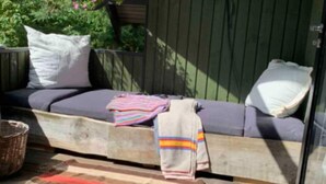 A cozy outdoor seating area with a wooden bench, cushions, and a striped blanket.