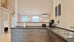 A modern kitchen with wooden panel walls, a central island with a sink, and a coffee machine. - 5 Star Holiday Home in Juelsminde (Horsens)
