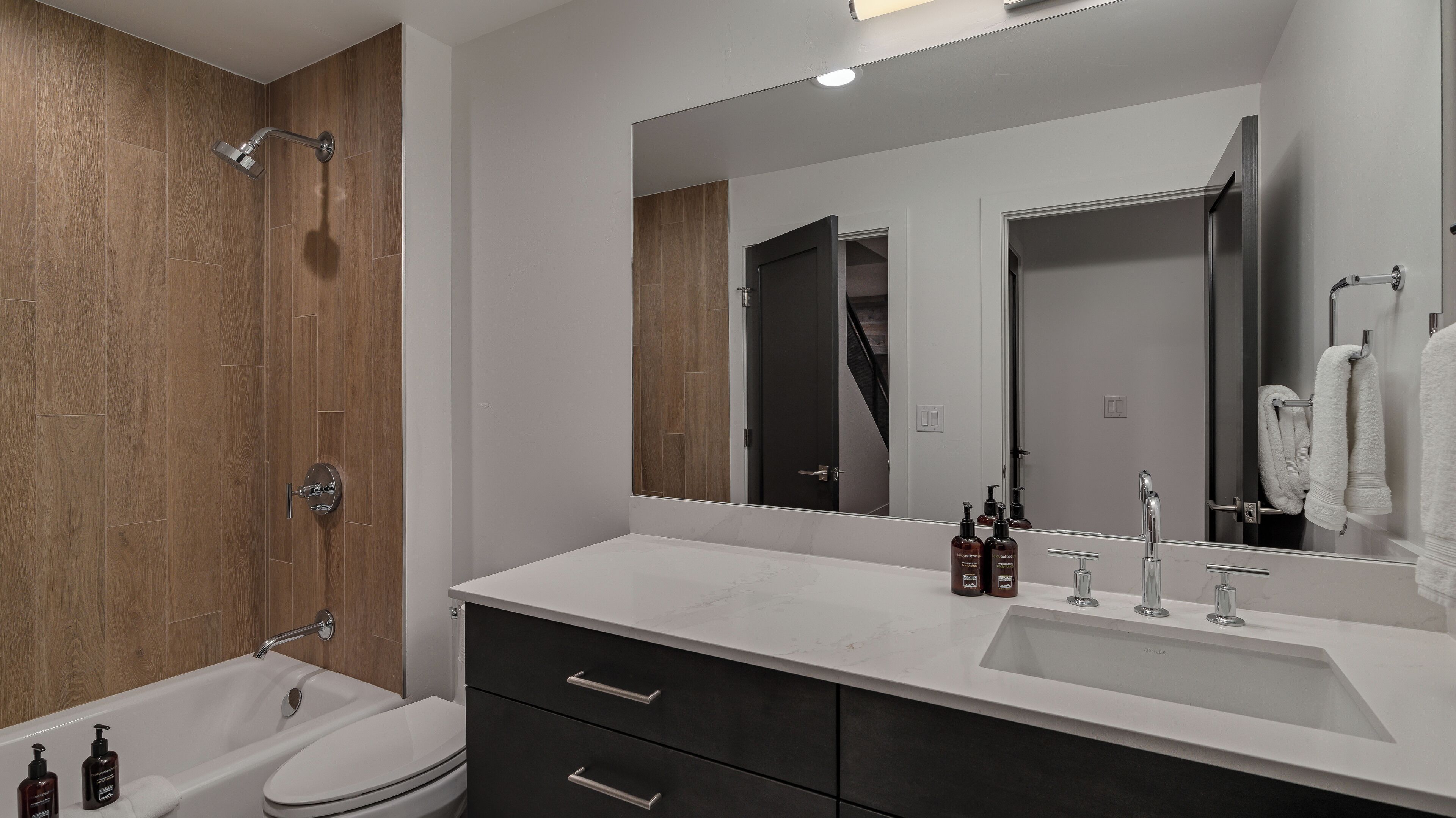 A modern bathroom with a bathtub, toilet, vanity with a sink, and a large mirror.