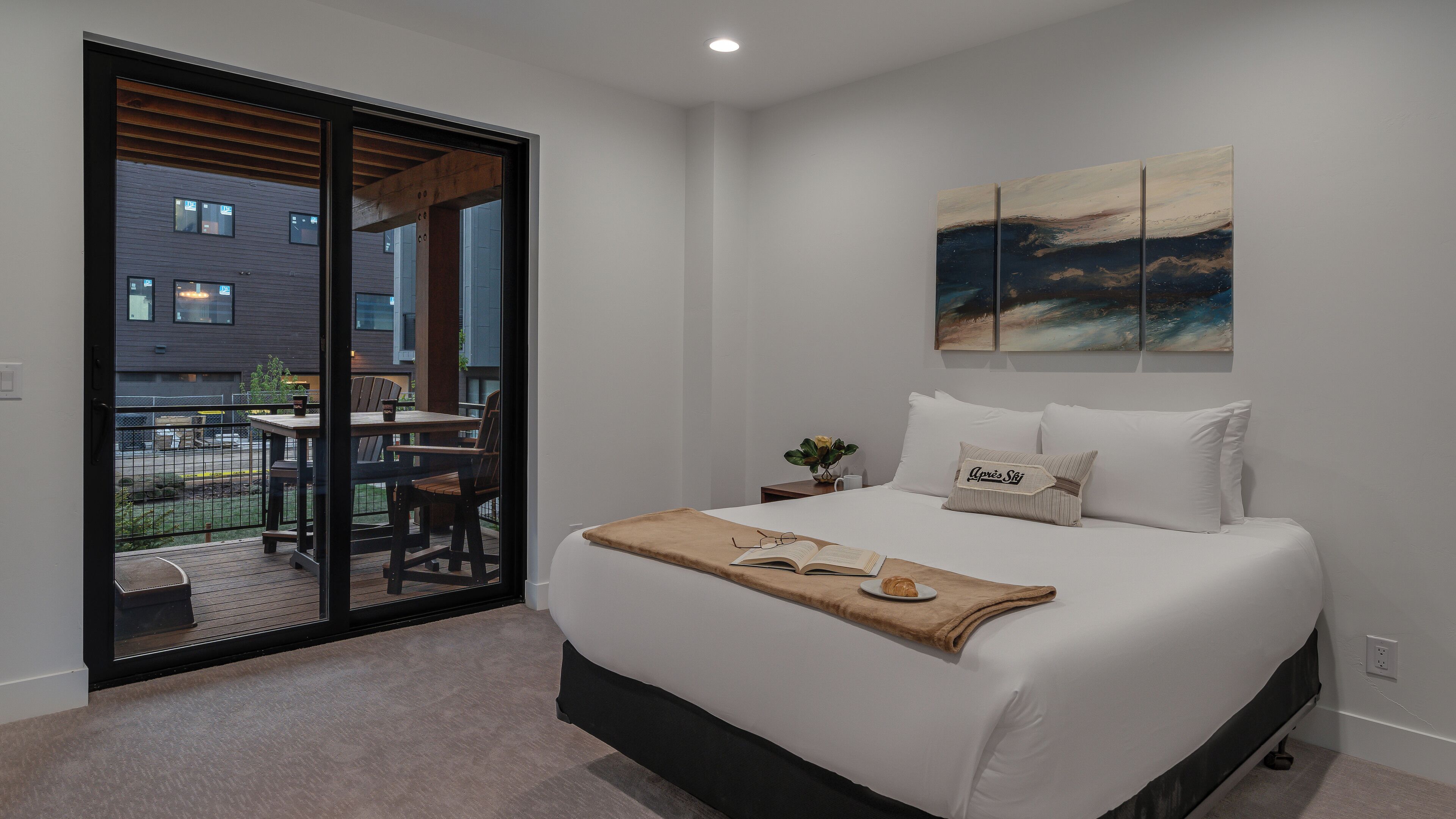 A bedroom with a large bed, a sliding glass door to a balcony, and a painting on the wall.