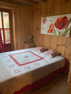 A wooden-paneled room with a bed, a window, and a painting.
