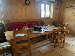 A wooden dining table with chairs, a red cushioned bench, and various dishes and glasses.