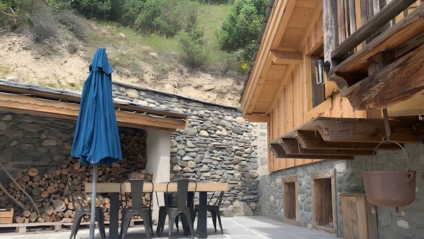 A stone building with a wooden exterior, a stone wall, and a table with chairs. - Chalet 'Saint Roch' with Mountain View, Private Terrace and Wi-Fi (Val-Cenis)