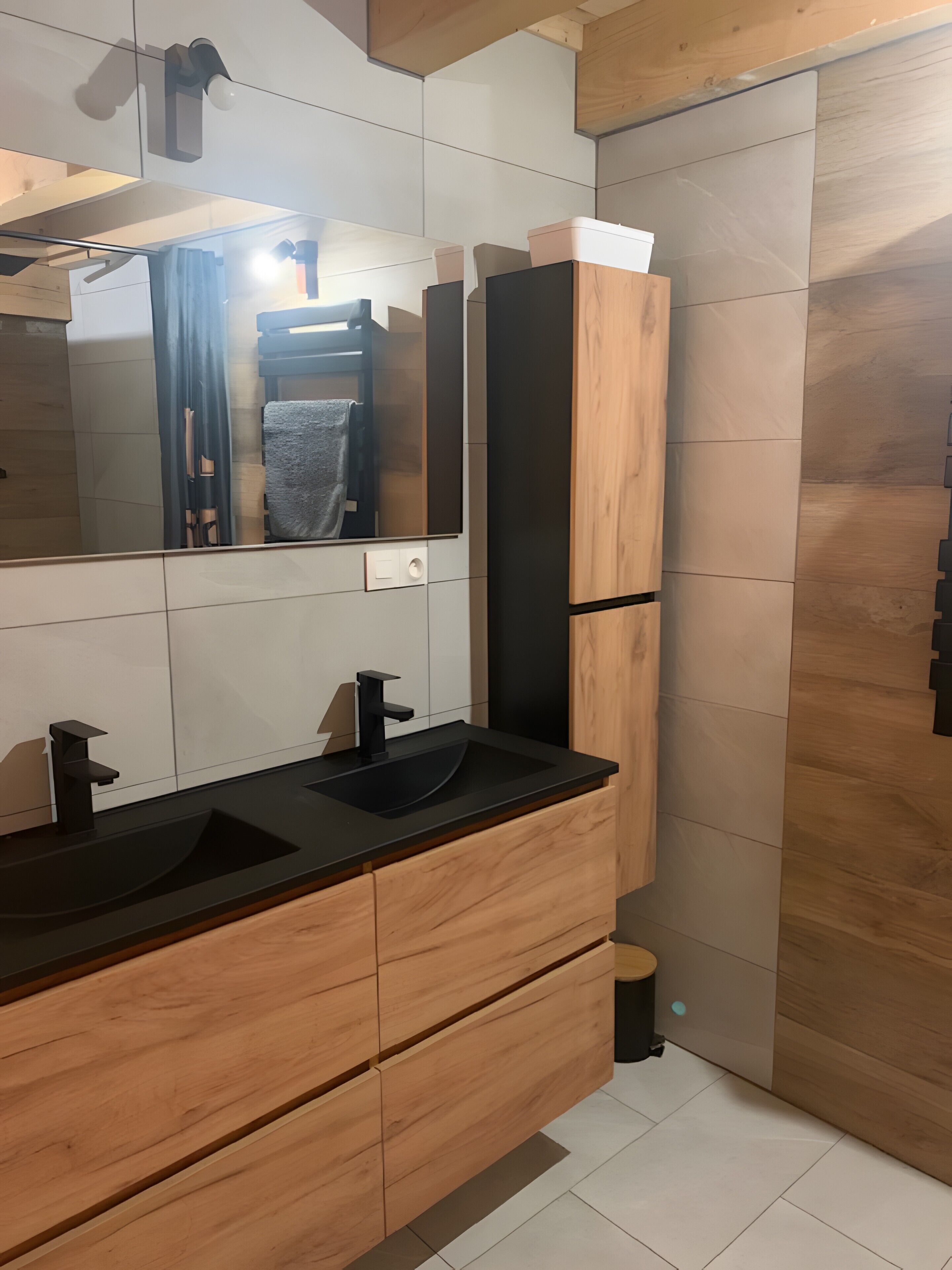 Ein modernes Badezimmer mit einem Holzwaschtisch, einem schwarzen Waschbecken und einem Spiegel.