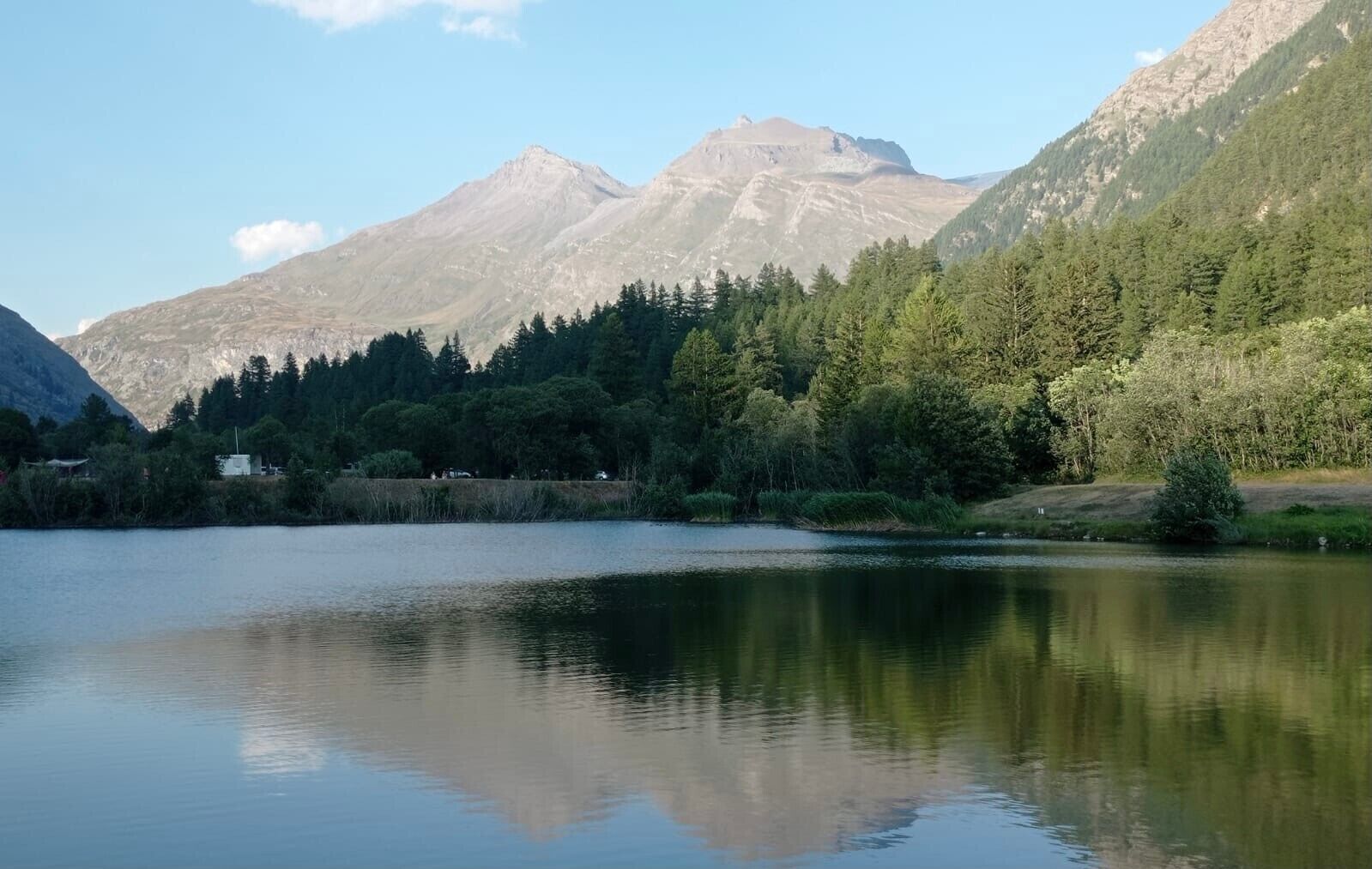 Ein ruhiger See mit Spiegelungen, umgeben von dichtem Wald und Bergen.