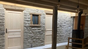A room with stone walls, wooden doors, a small window, a black stove, and a wooden ladder. - Chalet 'Saint Roch' with Mountain View, Private Terrace and Wi-Fi (Val-Cenis)