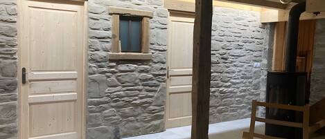A room with stone walls, wooden doors, a small window, a black stove, and a wooden ladder.